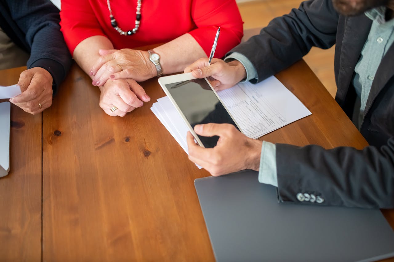 expertise-01 Business meeting at a wooden table with consultant reviewing documents and using a digital tablet.
